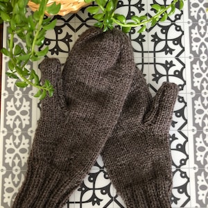 May include: A pair of brown knitted fingerless gloves with a ribbed cuff. The gloves are laid flat on a patterned surface.