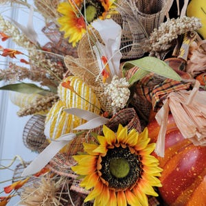 Puede incluir: Una corona de oto&ntilde;o con girasoles, arpillera y una peque&ntilde;a calabaza. La corona est&aacute; decorada con detalles marrones, amarillos y naranjas.