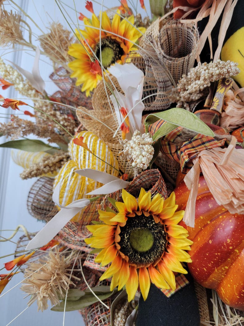 Puede incluir: Una corona de oto&ntilde;o con girasoles, arpillera y una peque&ntilde;a calabaza. La corona est&aacute; decorada con detalles marrones, amarillos y naranjas.