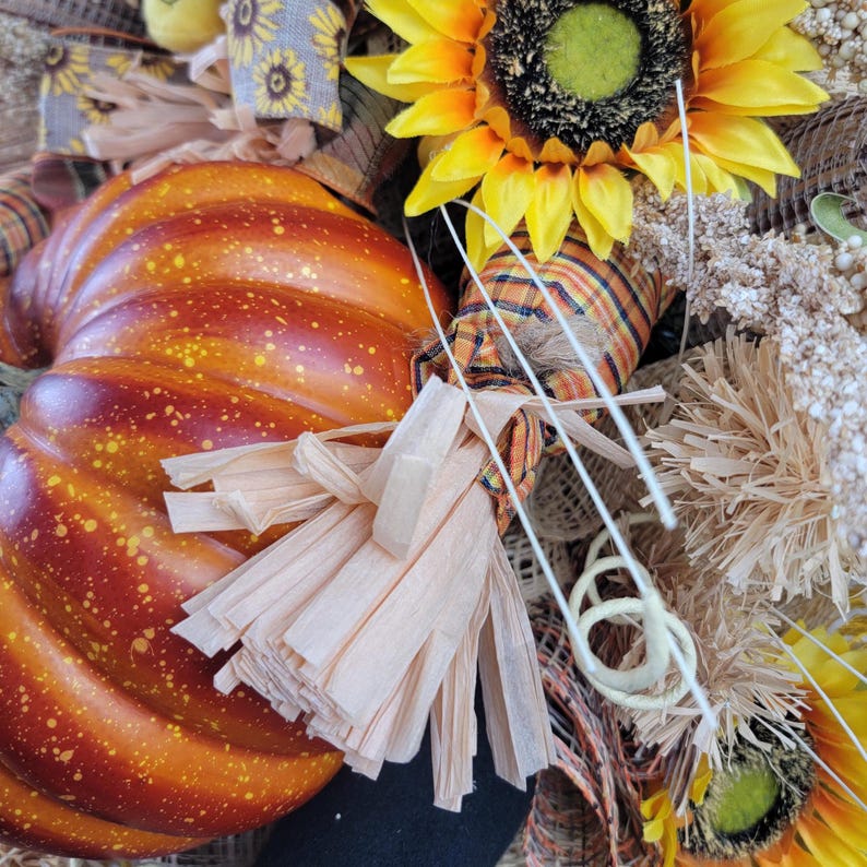 Puede incluir: Una corona de oto&ntilde;o con una calabaza naranja grande, un girasol y detalles de arpillera.
