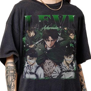 May include: Dark gray t-shirt featuring a graphic of Levi Ackerman from the anime series. The design includes multiple images of the character, the name "LEVI" in green, and the last name "Ackerman". The shirt has a vintage, distressed look.