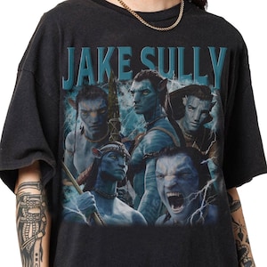 May include: Black t-shirt with a graphic of Jake Sully from Avatar. The design shows several blue Na'vi characters with lightning and the name "JAKE SULLY" in teal. A film-themed garment.