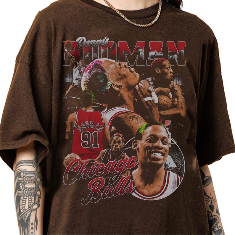 May include: Brown t-shirt with a collage of images of Dennis Rodman, with the text "Dennis Rodman" and "Chicago Bulls" in red and white. The shirt includes images of Rodman in a Chicago Bulls jersey.