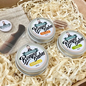 Könnte beinhalten: Ein Geschenkset für die Bartpflege enthält drei kleine Gläser Bartbalsam in den Duftrichtungen Orange, Limette und Vanille. Jedes Glas trägt ein Etikett mit dem Markennamen "DANIELS Beard Balm" und dem Duftnamen. Das Set enthält außerdem eine kleine Jutesack mit einem Knopf, auf dem "DANIELS GROOMING" steht, und einen Holzkamm.
