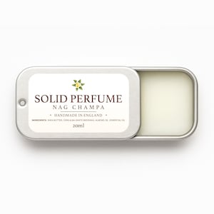 May include: A silver tin of solid perfume, open to show a pale yellow balm. The label reads "SOLID PERFUME NAG CHAMPA HANDMADE IN ENGLAND 20ml". Ingredients include shea butter, beeswax, almond oil, and essential oil. A floral graphic is also present.