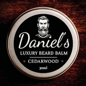 May include: A round, silver tin of Daniel's Luxury Beard Balm. The black label features a stylized illustration of a man with a beard and the text "Daniel's", "Cedarwood", and "30ml".