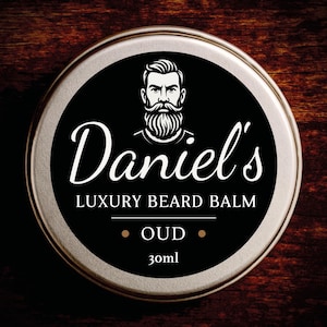 Könnte beinhalten: Eine runde, silberne Dose mit Daniel's Luxury Bartbalsam. Das schwarze Etikett zeigt eine stilisierte Illustration eines Mannes mit Bart und den Text "Daniel's" in weißer Schrift. Der Text "OUD" und "30ml" sind ebenfalls sichtbar.
