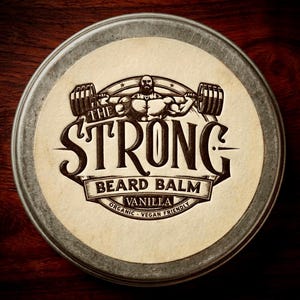 May include: A round metal tin with a cream-colored label featuring the text "THE STRONG BEARD BALM" and an illustration of a weightlifter. The label also includes the words "VANILLA", "ORGANIC", and "VEGAN FRIENDLY".