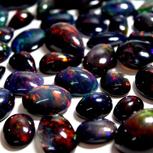 May include: A collection of polished black opal gemstones with smooth, rounded surfaces. Each stone features a dark base color with vibrant, iridescent flashes of red, green, blue, and orange light reflecting from within the cabochon-cut gems.