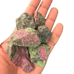 May include: A collection of raw ruby in zoisite mineral stones featuring a mottled texture with vibrant magenta-pink inclusions embedded within a dark forest green and black crystalline matrix, showcasing natural jagged edges and rough surfaces.