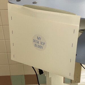 May include: A white paper sign with a blue circle and the text "MY DESK TOP BUDDY" on a white stand.