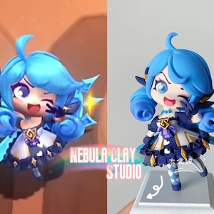 Può includere: Una statuetta blu e bianca di un personaggio con lunghi capelli blu, che indossa un vestito bianco e nero con un fiocco blu. La statuetta tiene un bastone blu e ha un'espressione ammiccante. La statuetta è in piedi su una base bianca con il testo "Nebula Clay Studio" e "木偶坊" sullo sfondo.