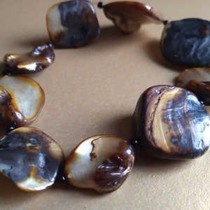 May include: A brown and white shell bracelet with black beads. The bracelet is made of large, irregularly shaped shells.