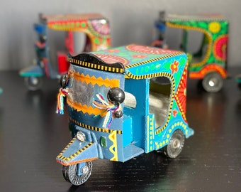 May include: Four colorful toy auto rickshaws, also known as tuk tuks, with intricate painted designs. The rickshaws are blue, green, red, and white with yellow, orange, and black accents.