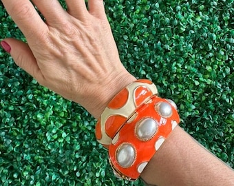 May include: Two orange and white bangle bracelets with a geometric pattern. The bracelets are stacked on a person's wrist.