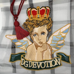 May include: A white mesh tote bag with an embroidered cherub angel design. The angel is wearing a crown and has wings. The bag has a black and white checkered pattern and the text "DG DEVOTION" is embroidered on the bottom.