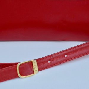 May include: A red leather shoulder bag with a gold buckle and a red leather strap.