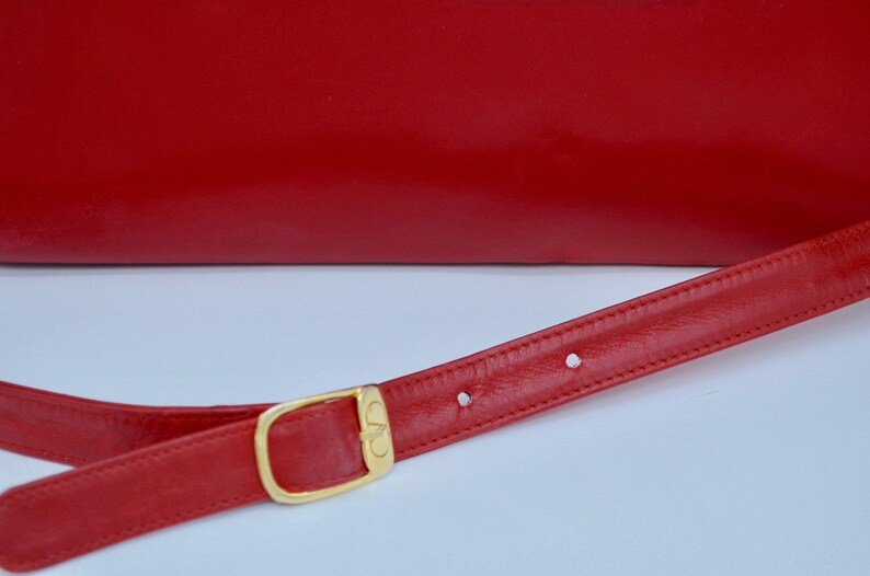 May include: A red leather shoulder bag with a gold buckle and a red leather strap.
