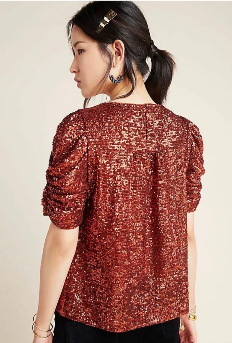 Pode incluir: Uma blusa de lantejoulas cor ferrugem com decote redondo e mangas curtas bufantes.