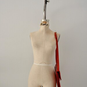 May include: A red leather shoulder bag with a long strap hanging on a white dress form.