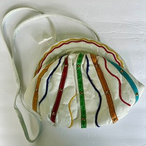 May include: White leather purse with a rainbow of colored stitching and gold accents. The purse has a long strap and a rounded shape.