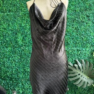 Puede incluir: Un vestido negro mini con cuello de pico y un patr&oacute;n de puntos blancos. El vestido tiene una correa halter y est&aacute; hecho de un material sedoso.