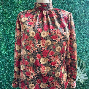 Könnte beinhalten: Eine langärmelige Bluse mit hohem Kragen und einem Blumendruck mit roten, gelben und grünen Rosen auf schwarzem Hintergrund.