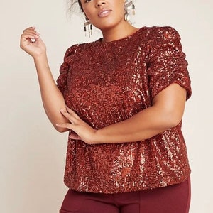 Pode incluir: Uma blusa marrom de lantejoulas com mangas bufantes curtas. A blusa tem um decote redondo e &eacute; feita de um tecido macio e confort&aacute;vel.