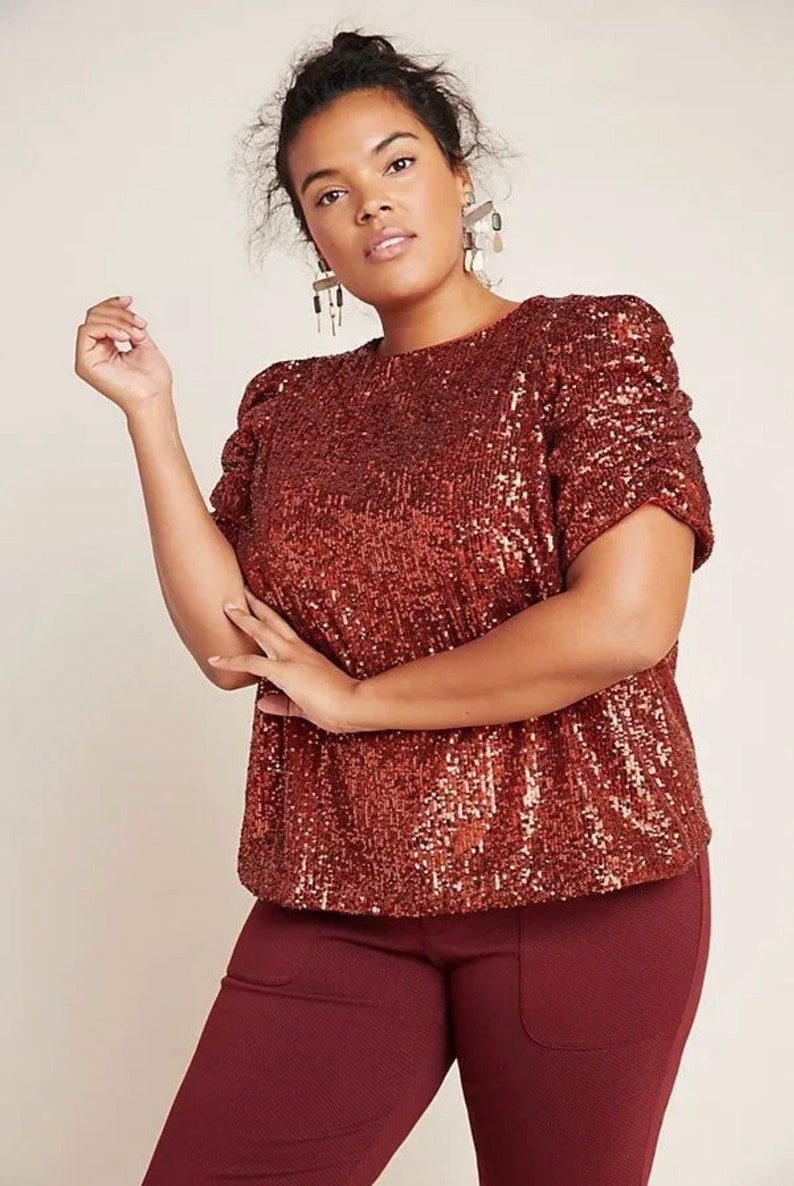 Pode incluir: Uma blusa marrom de lantejoulas com mangas bufantes curtas. A blusa tem um decote redondo e &eacute; feita de um tecido macio e confort&aacute;vel.