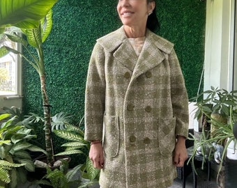 May include: A woman wearing a green and white plaid double-breasted coat with a pocket on each side. She is standing in front of a green wall.
