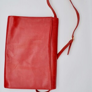 May include: A bright red leather shoulder bag with a long strap. The bag has a simple, rectangular shape and a flap closure.