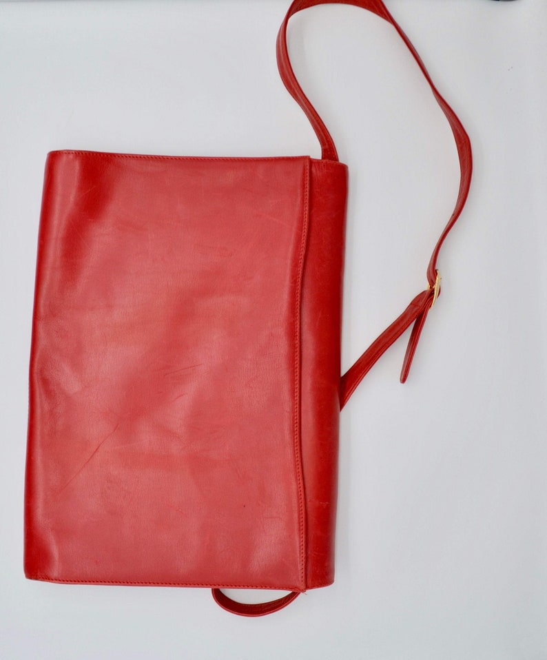 May include: A bright red leather shoulder bag with a long strap. The bag has a simple, rectangular shape and a flap closure.