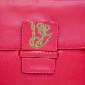 May include: A bright red leather handbag with a gold embroidered logo on the front flap.