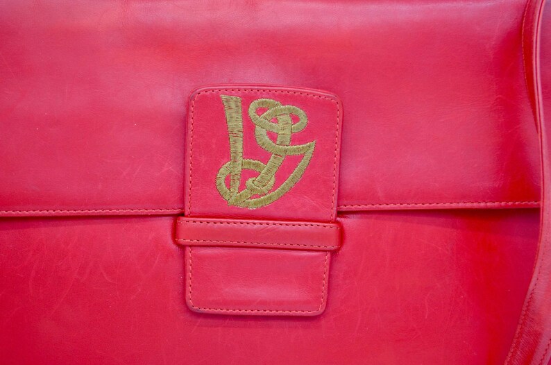 May include: A bright red leather handbag with a gold embroidered logo on the front flap.