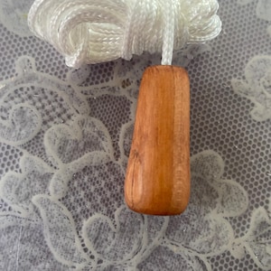 May include: A wooden light pull with a natural wood finish, attached to a white cord. The cord is coiled at the top. The pull is a simple, functional design.
