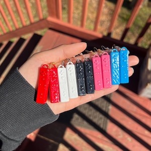 Puede incluir: Un conjunto de ocho pendientes de mando Nintendo Switch Joy-Con de colores. Los pendientes están hechos de plástico y tienen una superficie texturizada. Los colores incluyen rojo, blanco, negro, rosa, azul y azul claro.