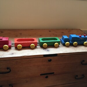 May include: A wooden toy train set with a blue engine, red, orange, and green cars. The engine has yellow wheels and the text "Playtime" on the side. The cars have yellow wheels and are connected by a metal chain.