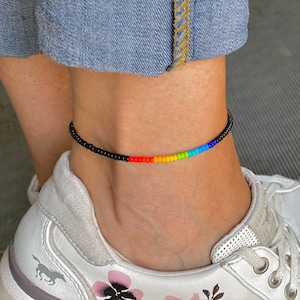Könnte beinhalten: Ein Regenbogen-Fußkettchen mit schwarzen Perlen. Das Fußkettchen besteht aus kleinen, bunten Perlen, die auf einer schwarzen Schnur aufgefädelt sind.