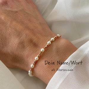 Könnte beinhalten: Ein Armband aus weißen Perlen und roségoldenen Perlen. Das Armband befindet sich am Handgelenk einer Person. Der Text "Dein Name/Wort als Morsecode" ist unterhalb des Armbands sichtbar.
