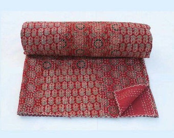 Op de afbeelding: Gerolde rood-gouden quilt met een gedetailleerd bloemmotief. De quilt is gedeeltelijk uitgerold en onthult de ingewikkelde stiksels en de achterkant. Het algemene thema is woondecoratie.