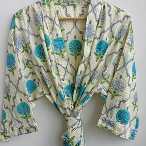 Könnte beinhalten: Eine cremefarbene Robe mit einem blauen und grünen Blumenmuster. Die Robe hat einen Bindegürtel und lange Ärmel.
