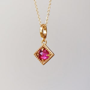 May include: A gold chain necklace with a pink gemstone pendant set in a gold, diamond-shaped frame.