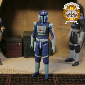 May include: A blue action figure of a character in a futuristic suit with a helmet, light blue accents, and a utility belt. The figure is holding a small black weapon. The Angry Raccoon Miniatures logo is in the upper right corner.
