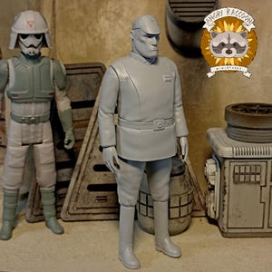 Peut inclure: Deux figurines grises de personnages d'une franchise de science-fiction. L'une porte un casque et une armure, l'autre est en uniforme avec une casquette. Les figurines sont dans une pièce avec des éléments de style industriel. Le logo Angry Raccoon Miniatures est visible.