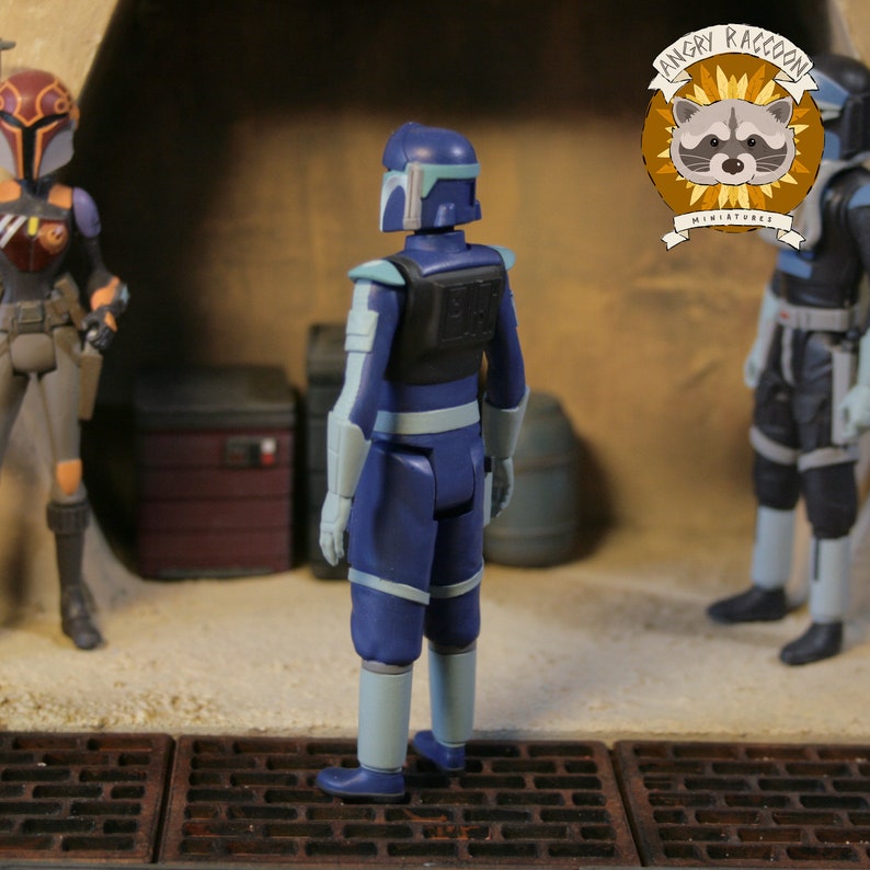 May include: A blue action figure of a character from a science fiction franchise, viewed from the back. The figure has light blue accents on the arms and legs, and a black vest. The figure is standing on a textured surface with other figures in the background.