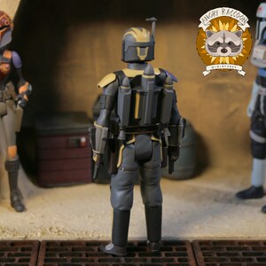 May include: A detailed action figure of a character in a gray and yellow armored suit, viewed from the back. The figure has a jetpack and holsters. The Angry Raccoon Miniatures logo is visible in the background.