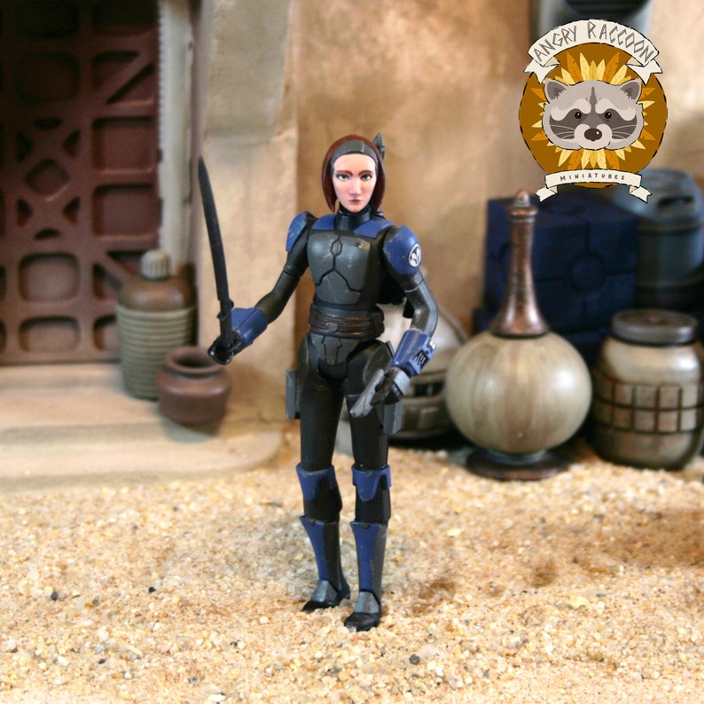 May include: A plastic action figure of a character with short dark hair, wearing black and blue armor with shoulder pauldrons and gauntlets. The figure holds a thin black sword in one hand and stands in a desert-like setting with various containers.