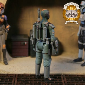 May include: A green and grey action figure of a science fiction character, seen from behind. The figure has a jetpack and other accessories. The Angry Raccoon Miniatures logo is visible in the background.