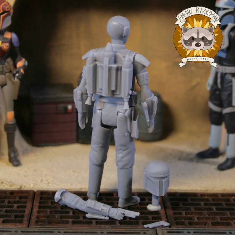 May include: A gray miniature figure of a character from a science fiction franchise, viewed from the back, with a jetpack and helmet. The figure is standing on a metal grate, with other figures and a logo in the background. The logo says "Angry Raccoon Miniatures".