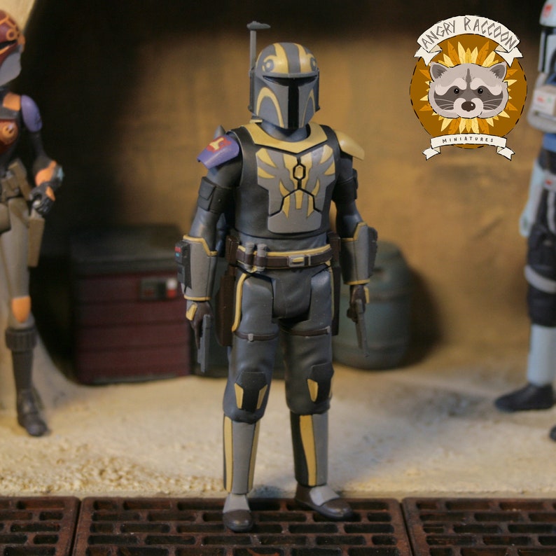 May include: A detailed action figure of a Mandalorian warrior in a gray and yellow color scheme. The figure is wearing armor with intricate designs, a helmet, and is holding a blaster pistol. The figure is part of a miniature collection.